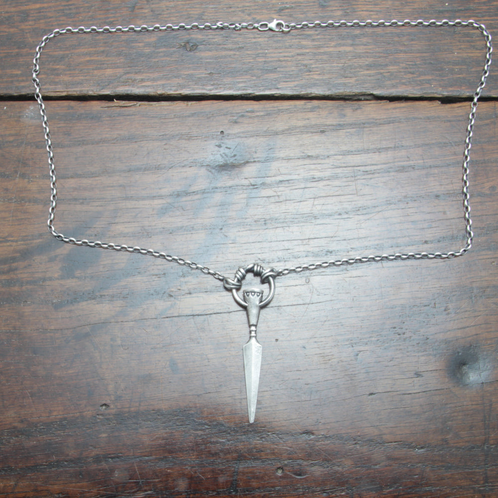 Flat lay of a silver spear pendant and chain, handcrafted by Taitaya Forge