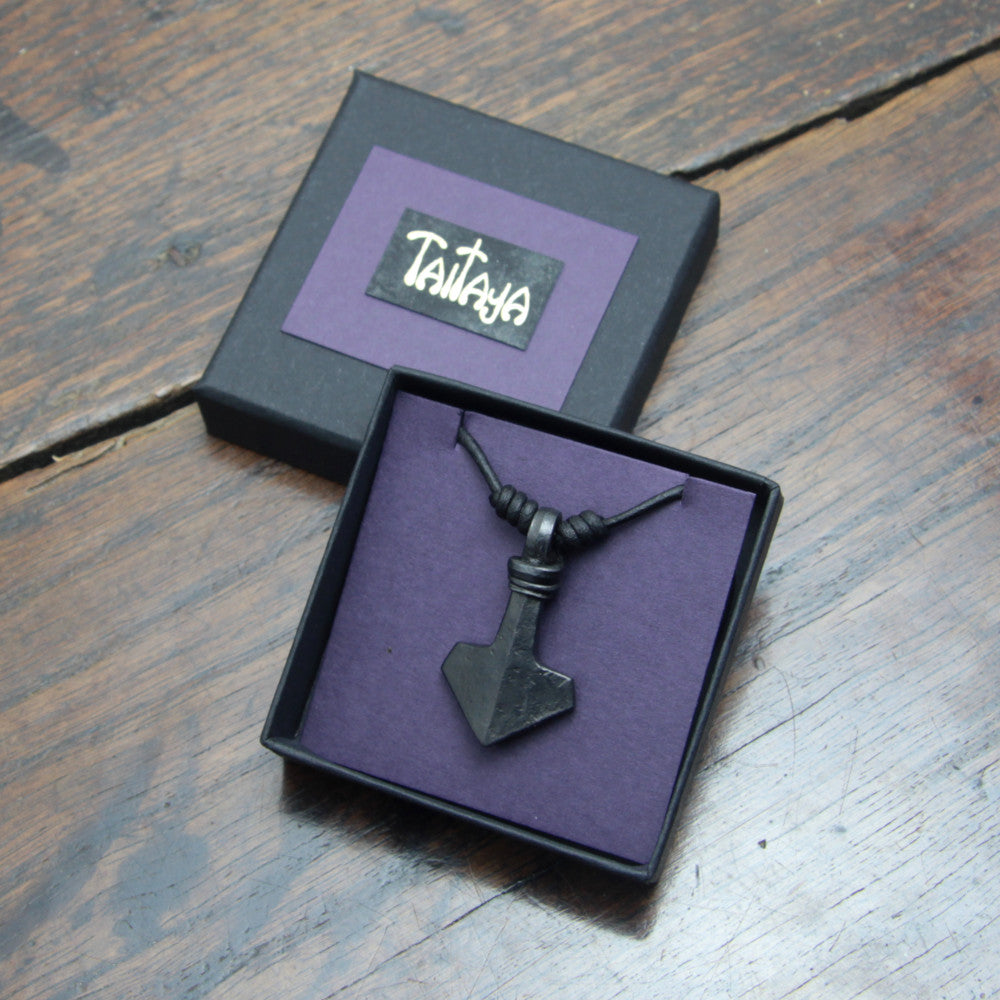 Handforged small ridged iron Mjolnir Thor's hammer pendant made by taitaya forge, presented in a black card gift box with gold embossed branding and purple insert card. 